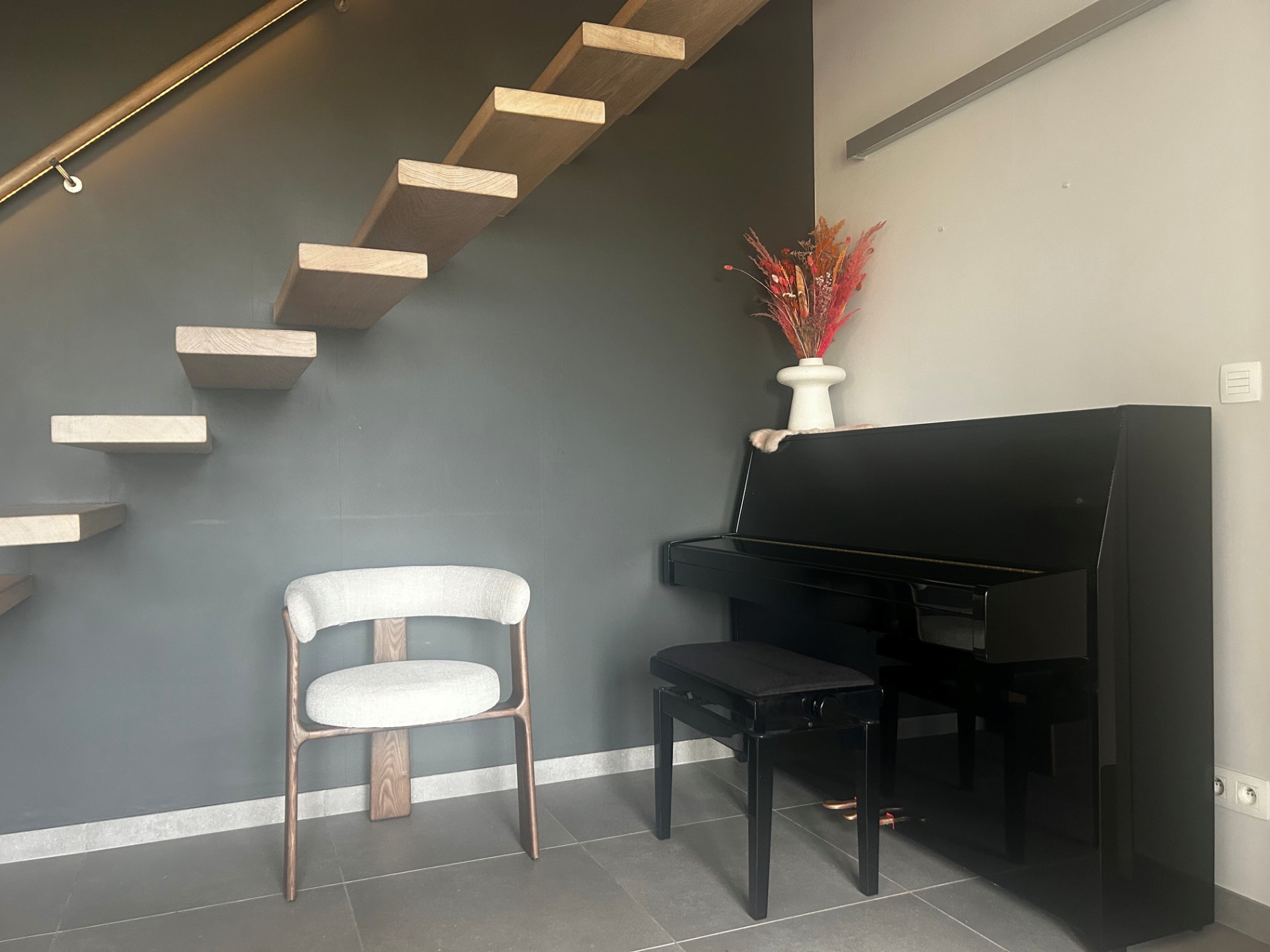 Een warme, lichte hoek in de praktijk met een stoel, piano en droogbloemen — een uitnodigende plek om samen te praten